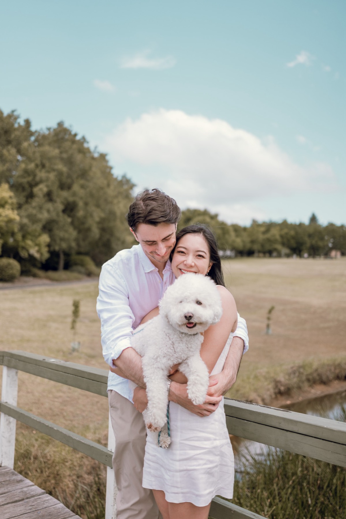 Damon hugging Christina from behind on a wooden bridge as she holds Marlo