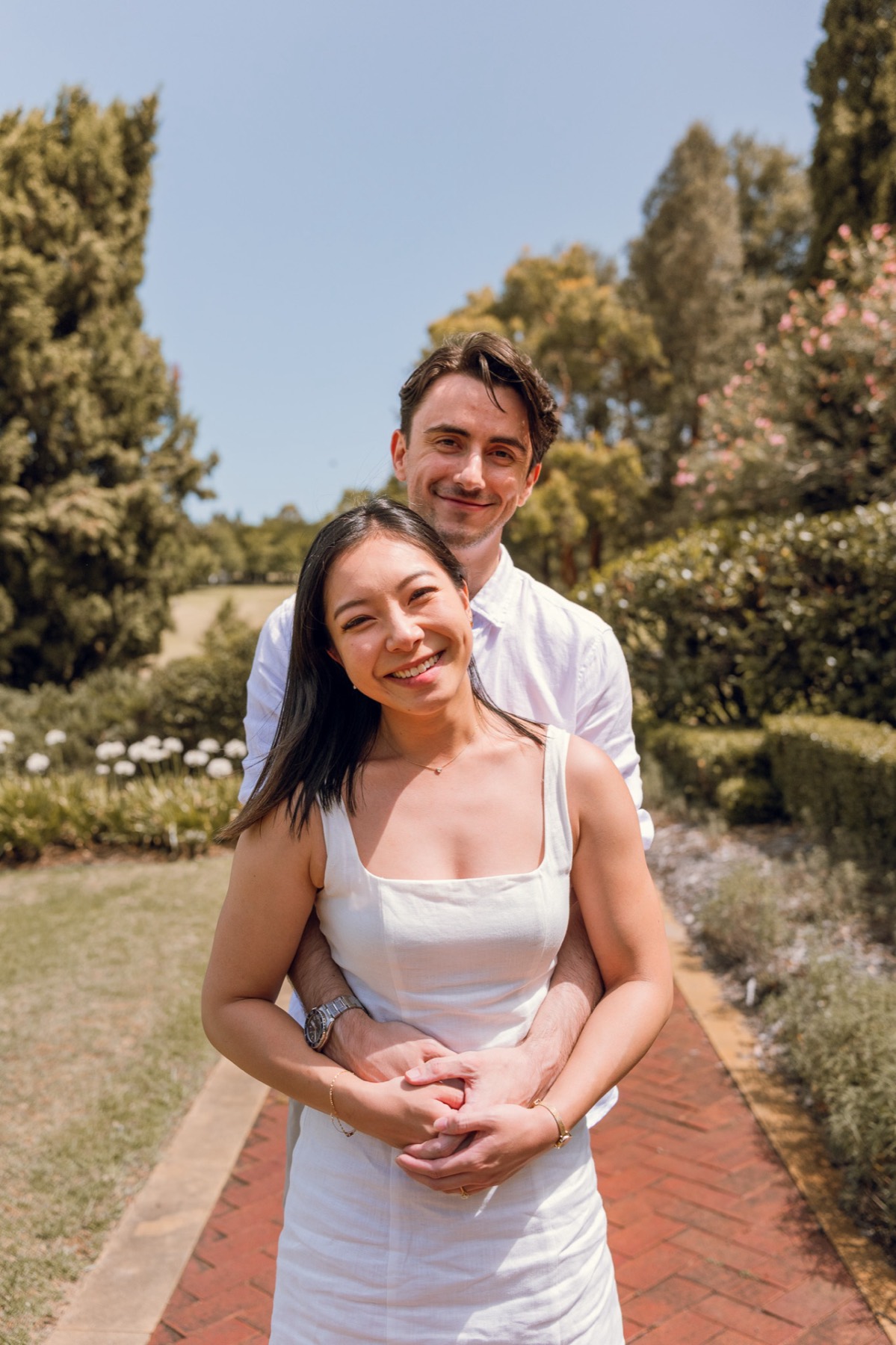 Christina laughing as Damon holds her from behind on a sunny garden path