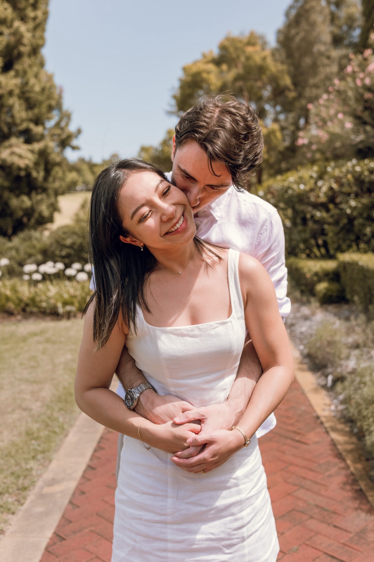 Damon kissing Christina's cheek from behind on a brick garden path