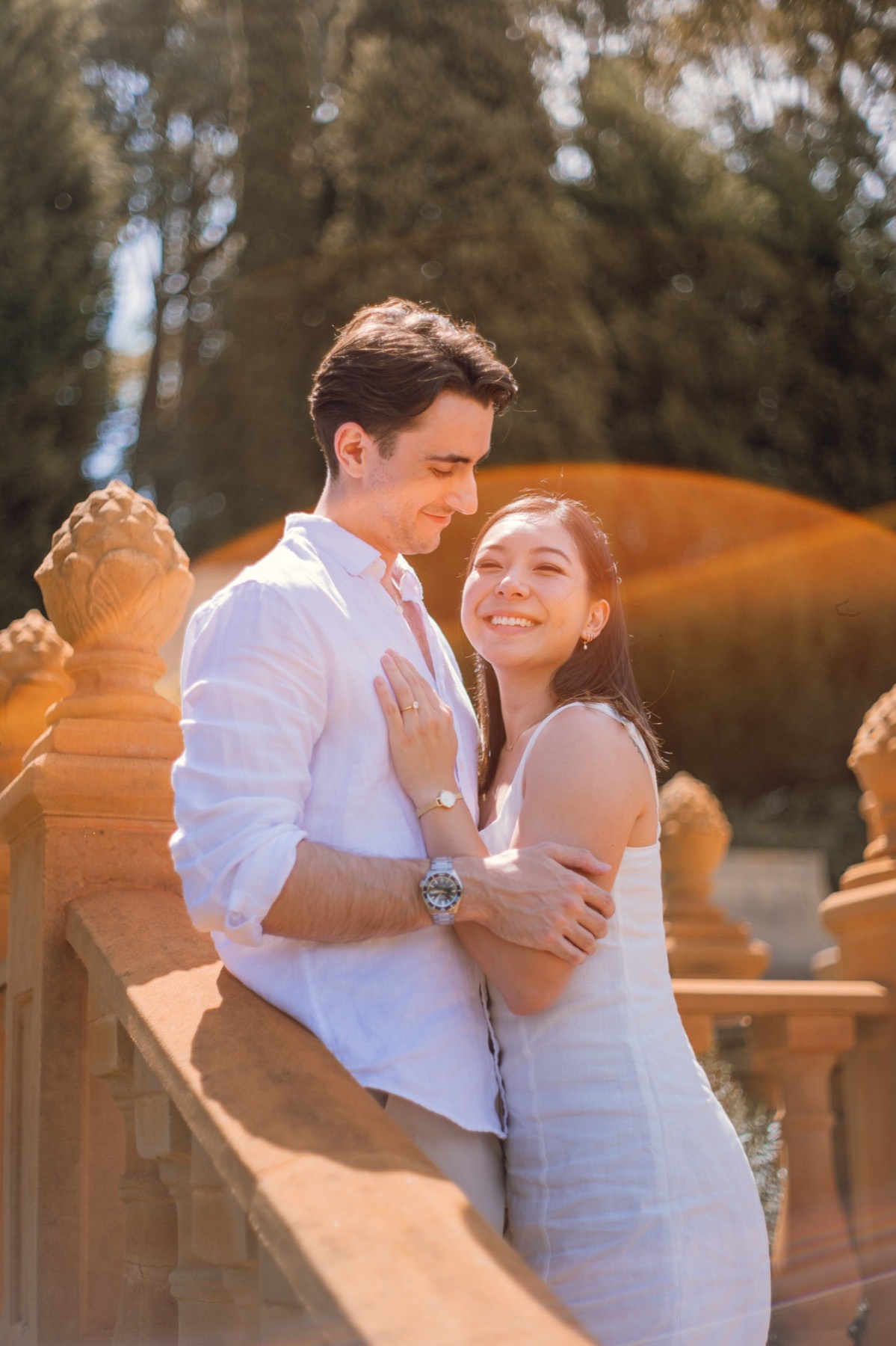 Christina smiling in Damon's arms at a sandstone balustrade, a warm light flare behind