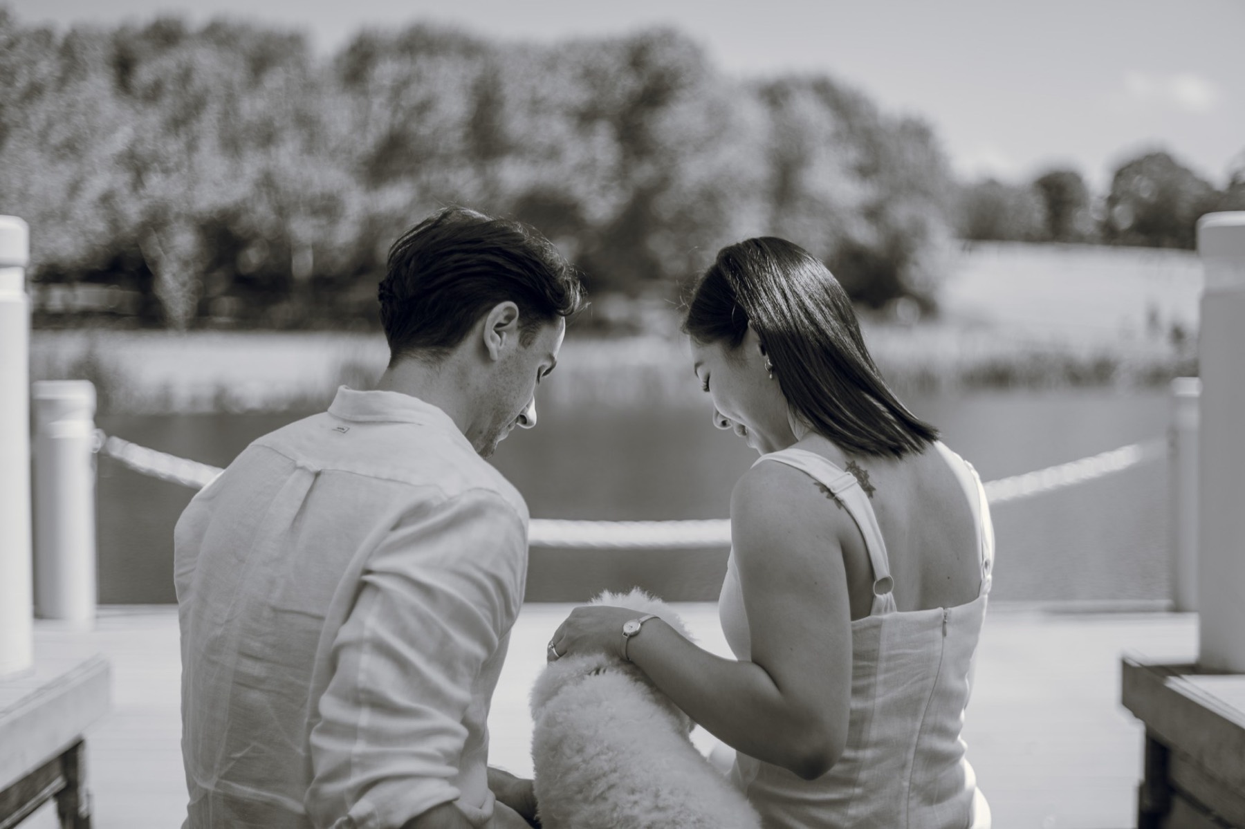 Black and white photo of the couple sitting by the lake, heads bowed over Marlo