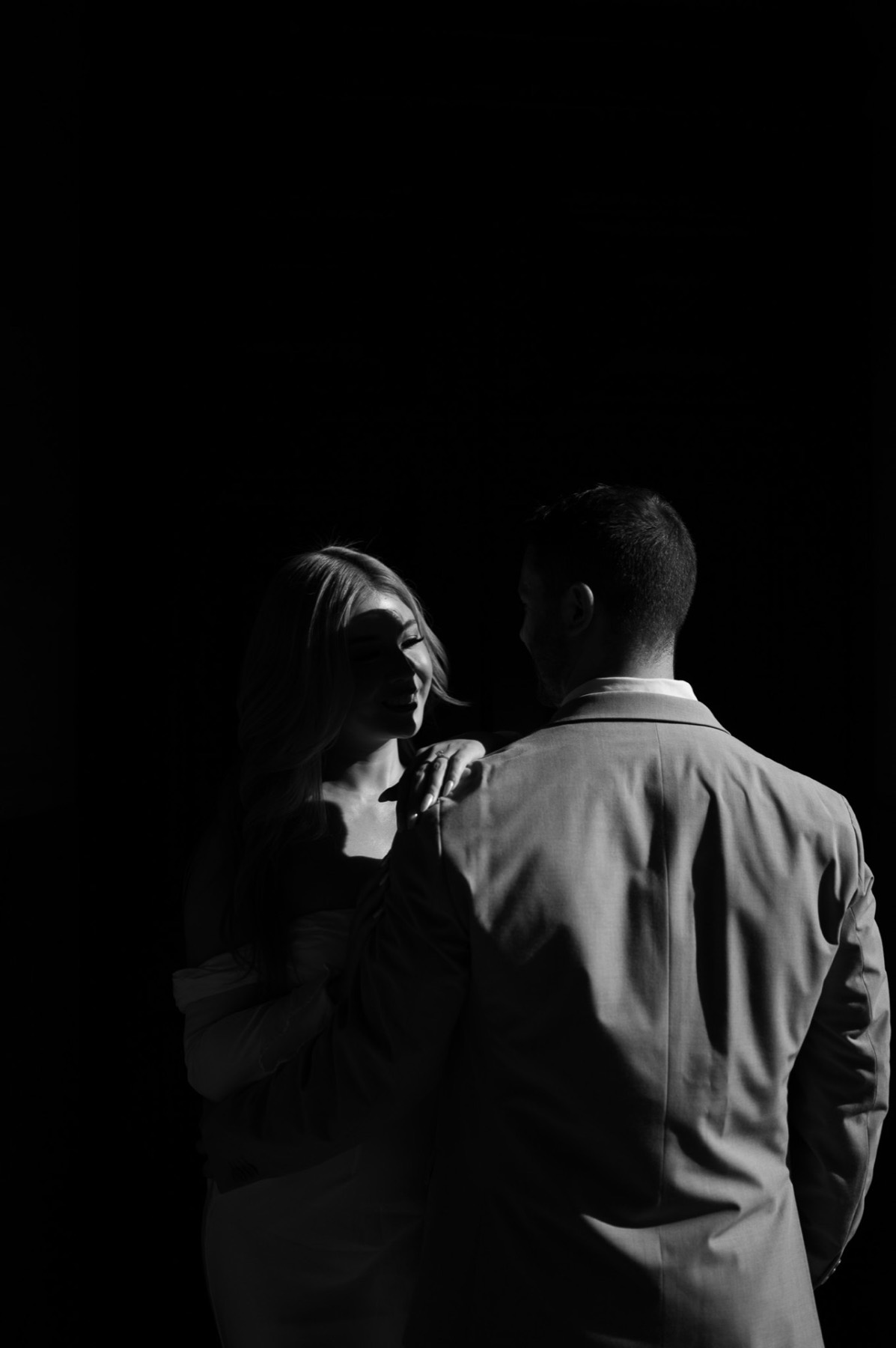 Black and white portrait of the couple in deep shadow, Kim's face lit by a thin strip of light
