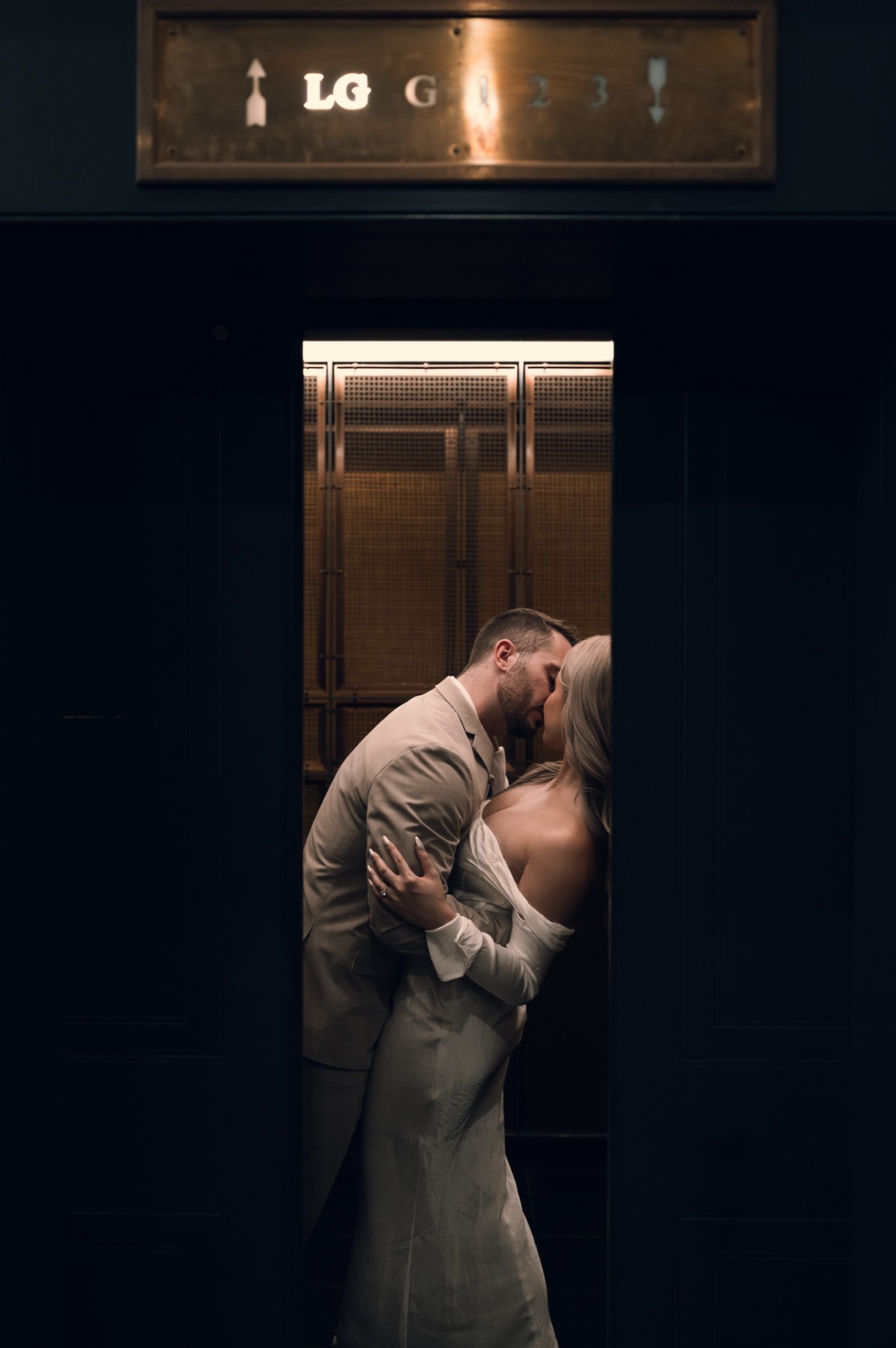 Dave and Kim kissing inside a lit elevator framed by a dark lobby