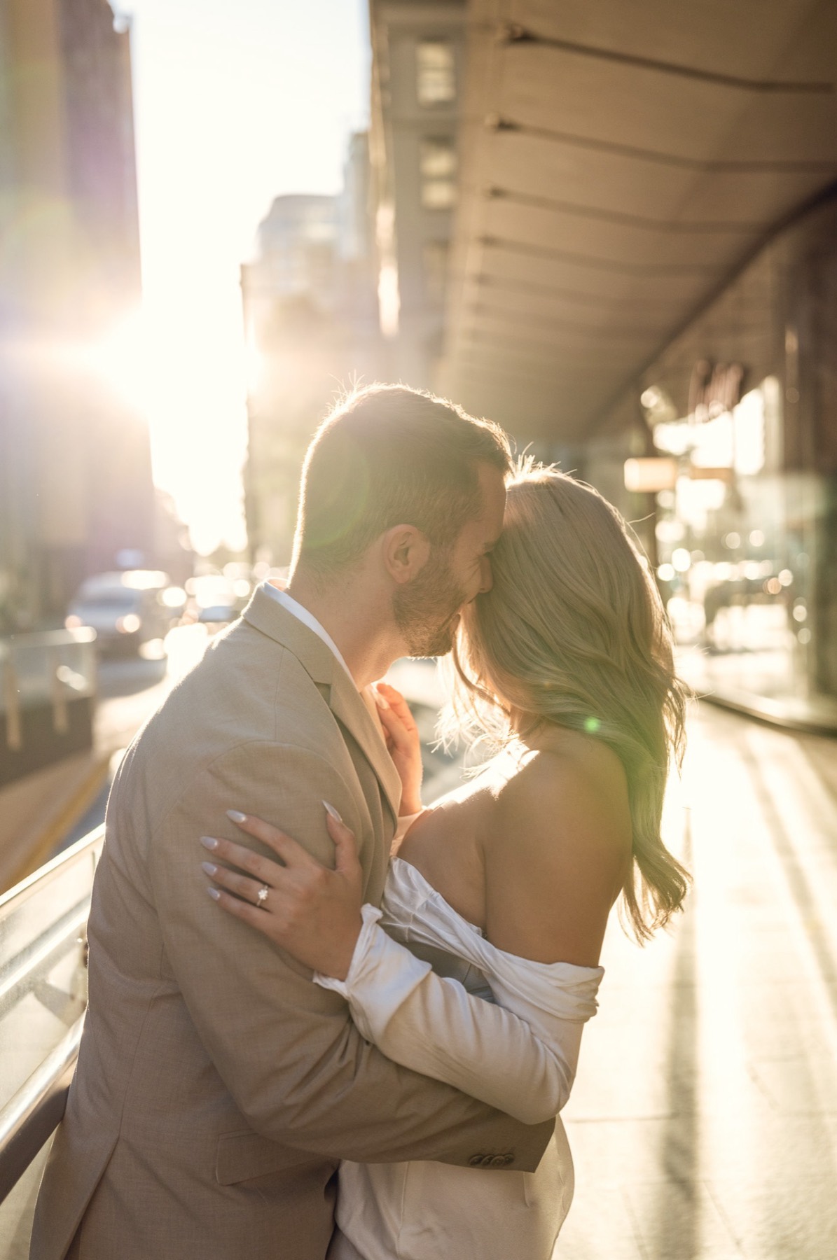 Dave kissing Kim's forehead on a sunlit city street, her hand on his back