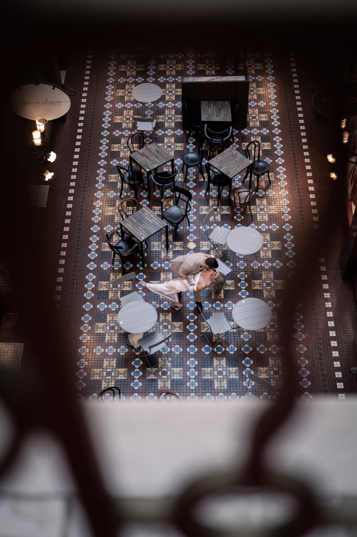 View from above of the couple dancing among café tables on a patterned tiled floor