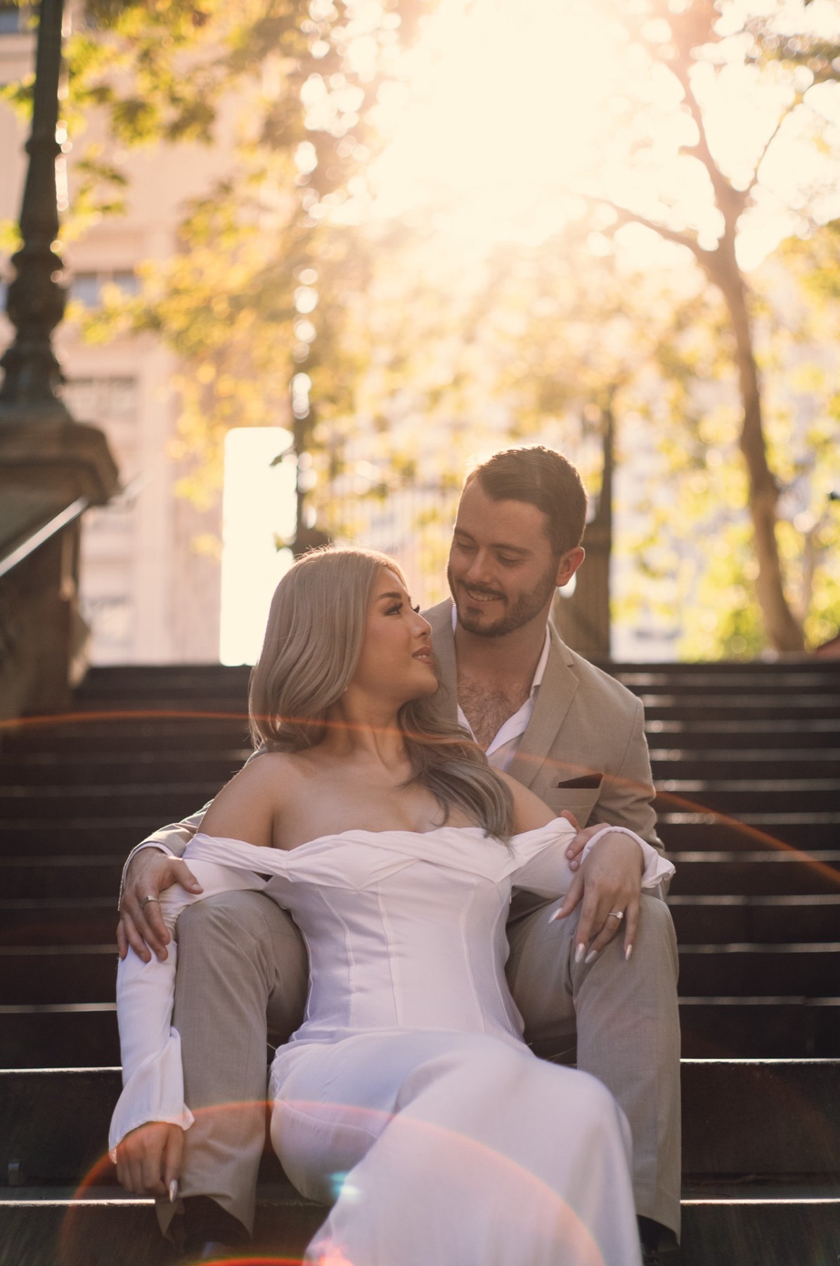 Kim sitting in Dave's arms on sandstone steps, trees and warm sun behind