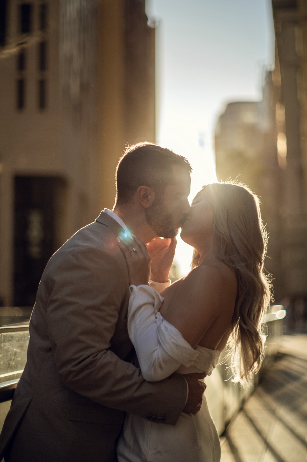 The couple kissing in golden light on a city bridge, sun flaring behind them