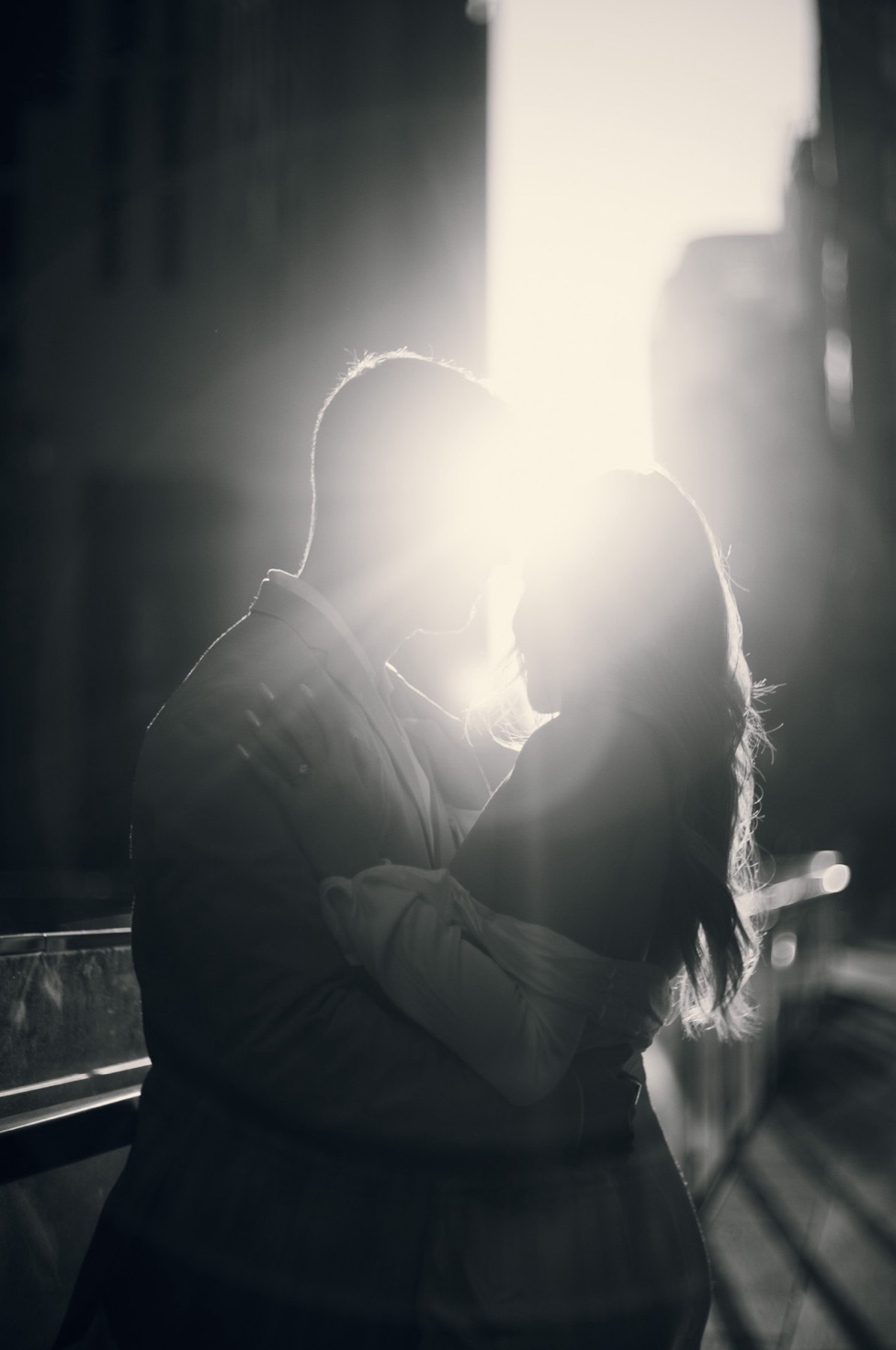 Black and white silhouette of the couple embracing, bright sun between buildings
