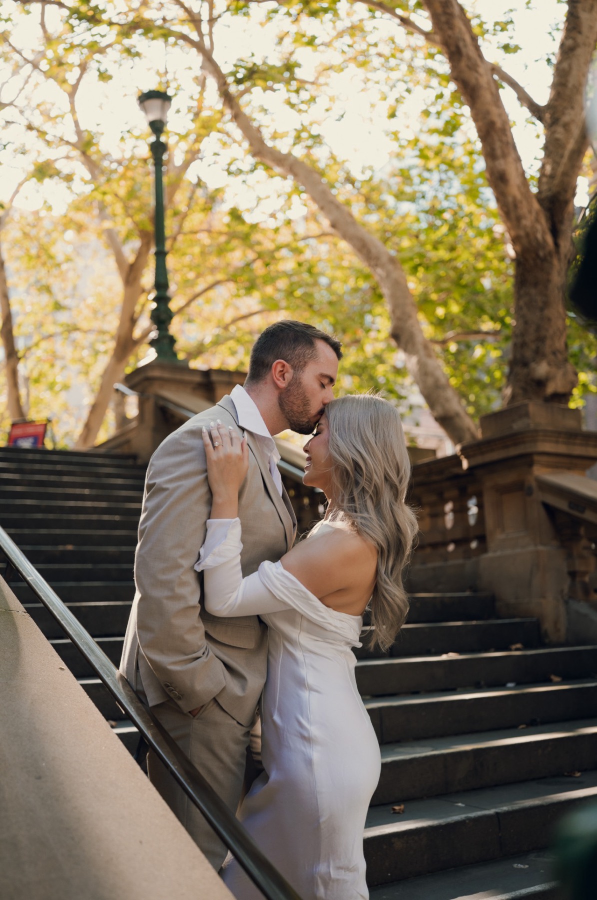 Dave kissing Kim's forehead on the sandstone stairs under autumn trees