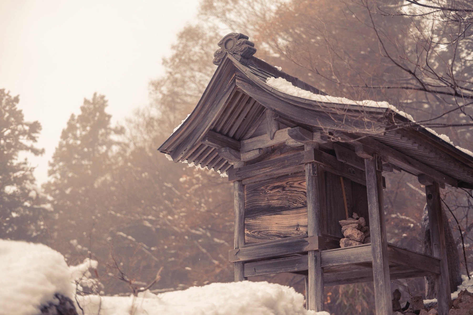 A small snow-covered wooden shrine in a misty forest