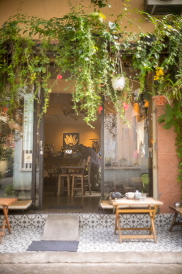 A plant-draped café doorway with patterned tiles and little wooden stools