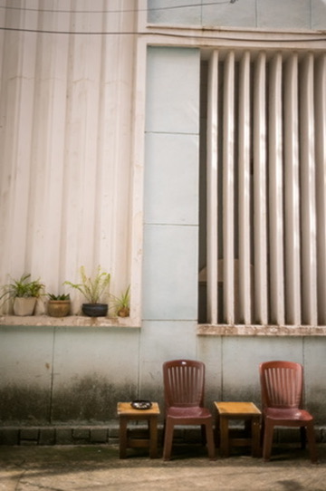 Two red plastic chairs and wooden stools against a pale ribbed wall