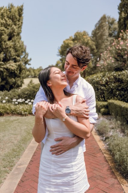 Christina laughing up at Damon as he wraps his arms around her in the garden