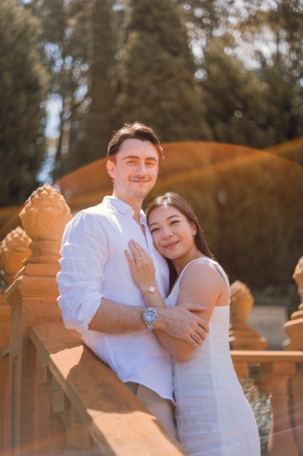 Damon and Christina smiling at the camera by a sandstone balustrade