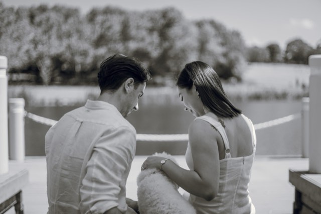 Black and white photo of the couple sitting by the lake, heads bowed over Marlo