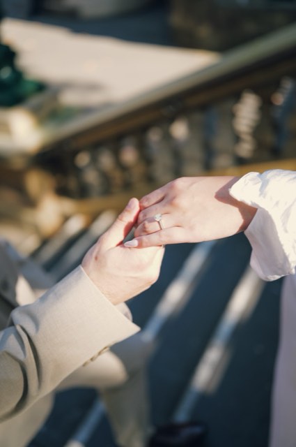 Close-up of Kim's hand with her engagement ring resting in Dave's hand beside a stone balustrade