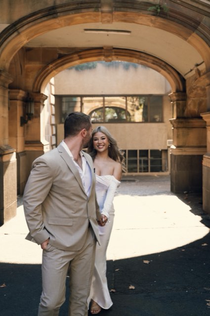 Kim smiling over Dave's shoulder as they walk out of a sunlit stone archway