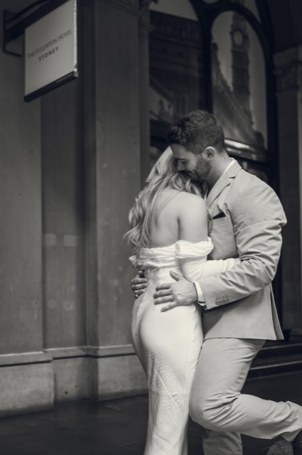 Black and white photo of Dave pulling Kim close under a hotel sign on a city street