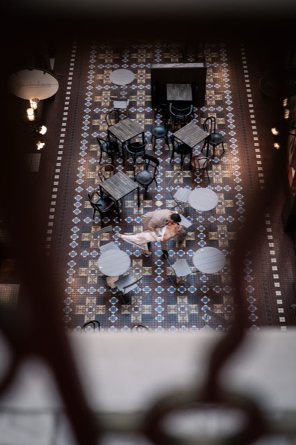 View from above of the couple dancing among café tables on a patterned tiled floor