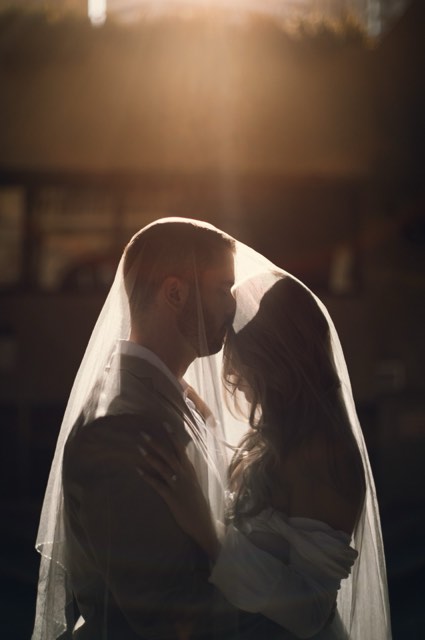 The couple kissing beneath Kim's veil, backlit so the veil glows
