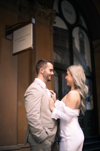 Dave and Kim laughing face to face beneath a hotel sign by an arched window