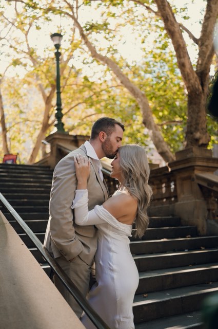 Dave kissing Kim's forehead on the sandstone stairs under autumn trees
